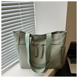 Detail of light green nylon tote bag featuring woven decorative cords and side pockets