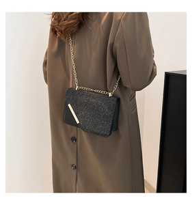 Detail of black glitter crossbody bag with gold metal trim and elegant chain strap