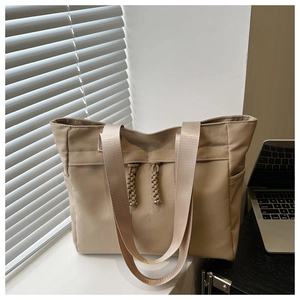 Large beige tote bag with drawstring details and dual handles in a bright minimalist office setting