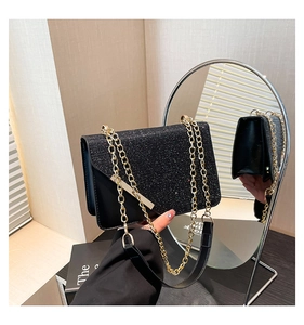 Detail of black glitter envelope bag with gold chain and sleek metallic bar accent