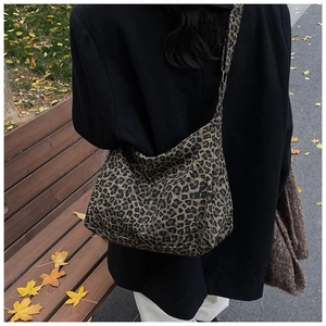 Leopard print canvas bag with wide strap shown on a woman sitting outdoors on a wooden bench