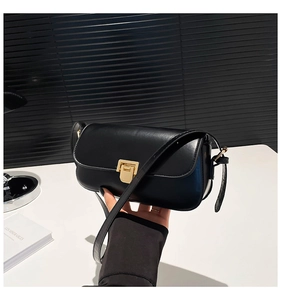 Detailed close-up of a black leather crossbody bag with a polished gold rectangular clasp