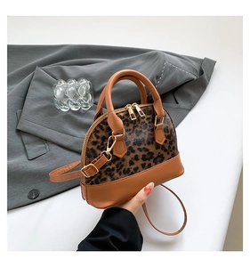 Detail of leopard print handbag featuring brown leather trim and golden zipper closures
