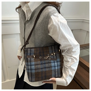 Detail of wool plaid bucket bag with brown leather accents and gold buckle details