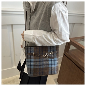 Detailed close-up of retro plaid bucket bag with brown leather trim and golden hardware