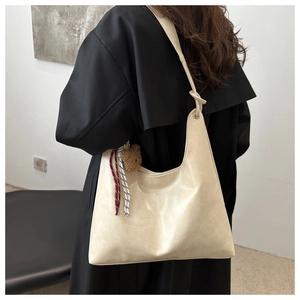 Détail du sac hobo crème avec breloque ours et bandoulière nouée porté par le mannequin