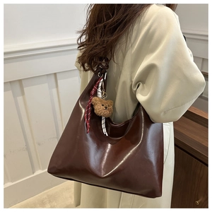 Gros plan d'un grand sac cabas en cuir marron brillant avec charme ours et bandoulières tissées