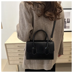 Close-up of black leather handbag with gold hardware styled on a grey blazer outfit