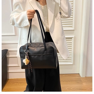 Close-up of a large black shoulder bag with a unique baseball charm on a white blazer