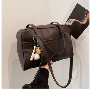 Detail of dark brown leather tote bag with baseball pendant and sleek shoulder straps