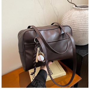 Close-up of deep brown commuter shoulder bag with a creative baseball pendant on a table