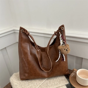 Sac hobo en cuir marron avec breloque ours sur un fond en tricot douillet et chaud