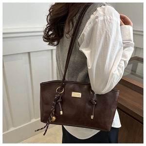 Close-up of dark brown leather tote bag with gold logo and woven rope charm detail