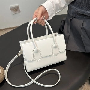 Minimalist white leather handbag featuring geometric patches and adjustable shoulder strap