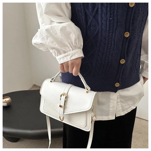 Side view of white crossbody bag with gold buckle and top handle in home setting
