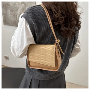 Detail view of woven texture and irregular flap design on brown crossbody bag worn by model