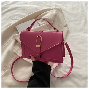 Detailed shot of fuchsia crossbody bag with golden U-shaped buckle on white bedding