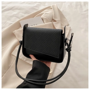 Detail of black woven texture on flap shoulder bag with smooth body held by hand