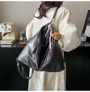 Detail of vintage black leather tote featuring dual zippers and cute bear charm