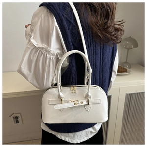 Rear view of a model carrying the white leather bowling bag with gold hardware and strap