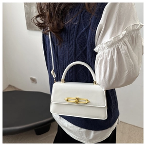 Detail view of the elegant golden metal bar lock and flap closure on white crossbody bag