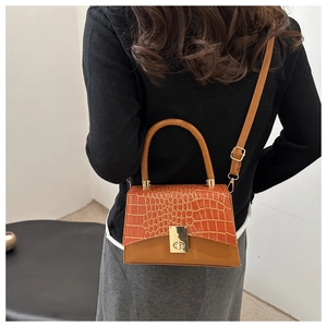 Detail of orange crocodile embossed flap bag with gold twist lock on shoulder strap