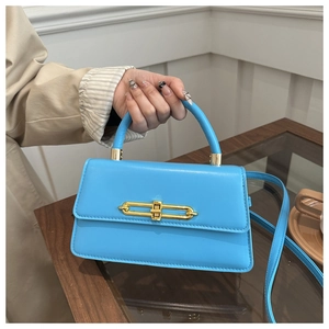 Detail of light blue faux leather crossbody bag with gold hardware on a wooden table