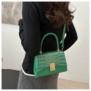 Detailed side view of green crocodile embossed handbag with gold buckle on a model