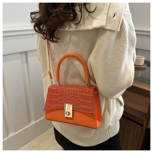 Detail der orangefarbenen Tasche mit Krokodilprägung, Metallschloss und Rundgriff