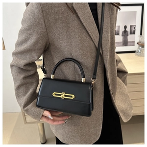Detail of black leather crossbody bag with gold metal link buckle on a textured blazer
