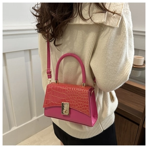 Detail der fuchsia Kroko-Ledertasche mit goldener Schließe auf einem beigen Pullover