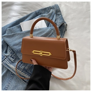 Detail of a brown leather crossbody bag with a gold metal bar buckle and rounded handle