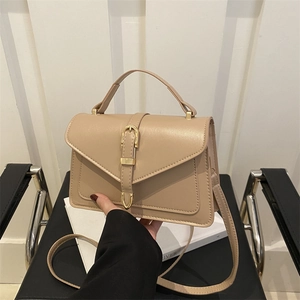 Beige faux leather crossbody bag with gold horsebit buckle held in a lifestyle setting