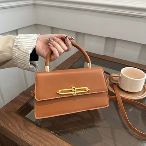 Elegant caramel brown leather crossbody square bag with gold buckle on a wooden table