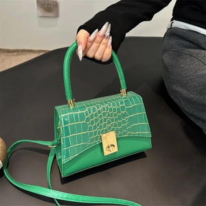 Structured emerald green crossbody bag with gold crocodile texture and metallic twist lock