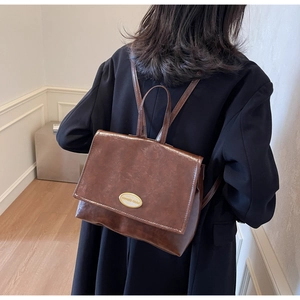 Close-up of a vintage brown oil-wax leather backpack featuring a golden oval metal buckle