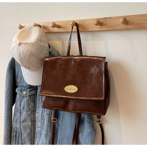 Detail of vintage oil wax leather backpack with gold emblem against minimalist wall