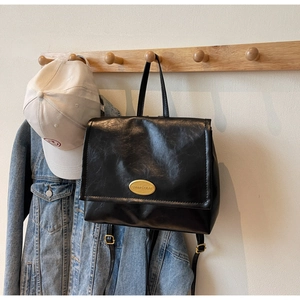 Detail of black oiled leather backpack featuring a gold oval plaque on the flap cover