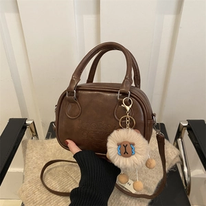 Dunkelbraune Boston-Tasche aus Leder mit Logoprägung und Anhänger in der Hand