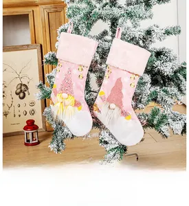 Pink plush Christmas stockings with glowing gnomes and gold sequins on a snow-covered tree