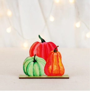 Three colorful wooden pumpkin desk ornaments with warm bokeh lights for fall harvest decor