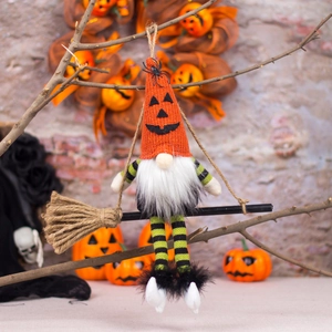 Halloween gnome doll hanging on a broom with pumpkin hat and spider detail on stone wall