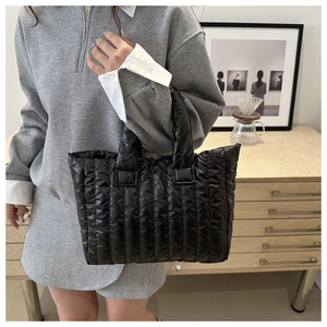 Close-up of black quilted puffer tote bag featuring vertical seams and padded handles