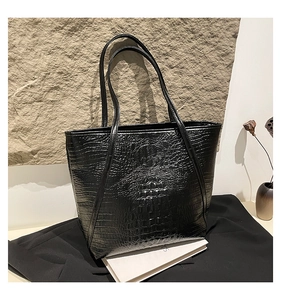 Detail of black faux crocodile pattern tote bag featuring embossed texture and slim straps