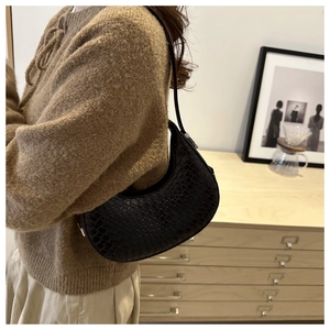 Close-up of black crocodile pattern faux leather half-moon hobo bag on a model's shoulder