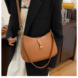 Detailed view of a brown crescent shoulder bag with gold clasp on a fashion model