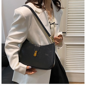 Detail of a vintage black crescent bag with a gold clasp worn over a white suit