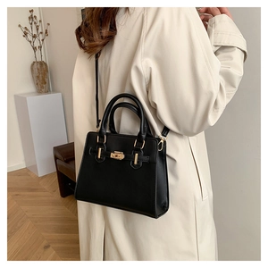 Close-up of black leather handbag with gold turn-lock closure and elegant strap detail