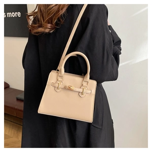 Beige faux leather handbag with gold buckle shown on a model in a black long coat