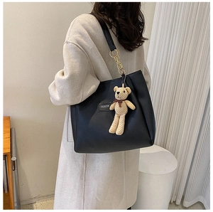 Detail of a large black tote bag with gold chain strap and a brown teddy bear charm